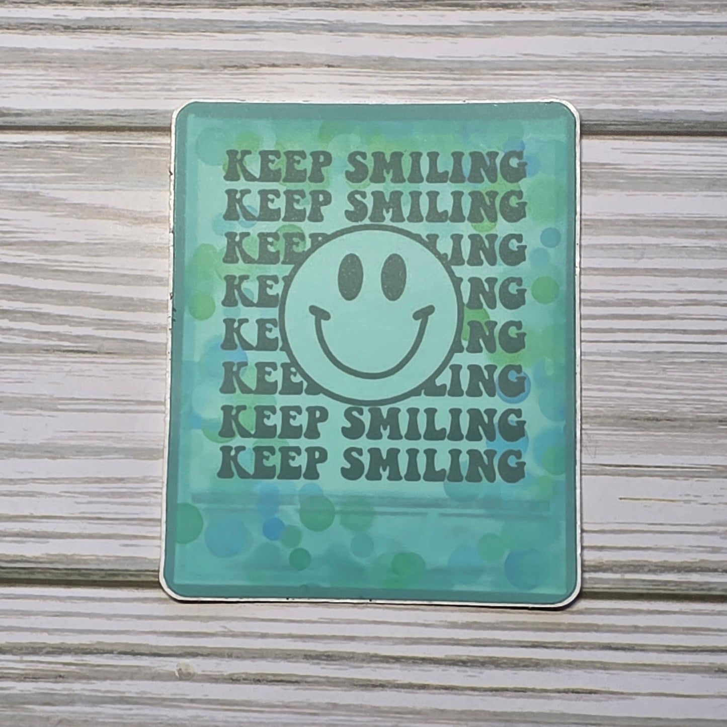 Teal Polaroid with the words Keep Smiling and a smiley face in frame.