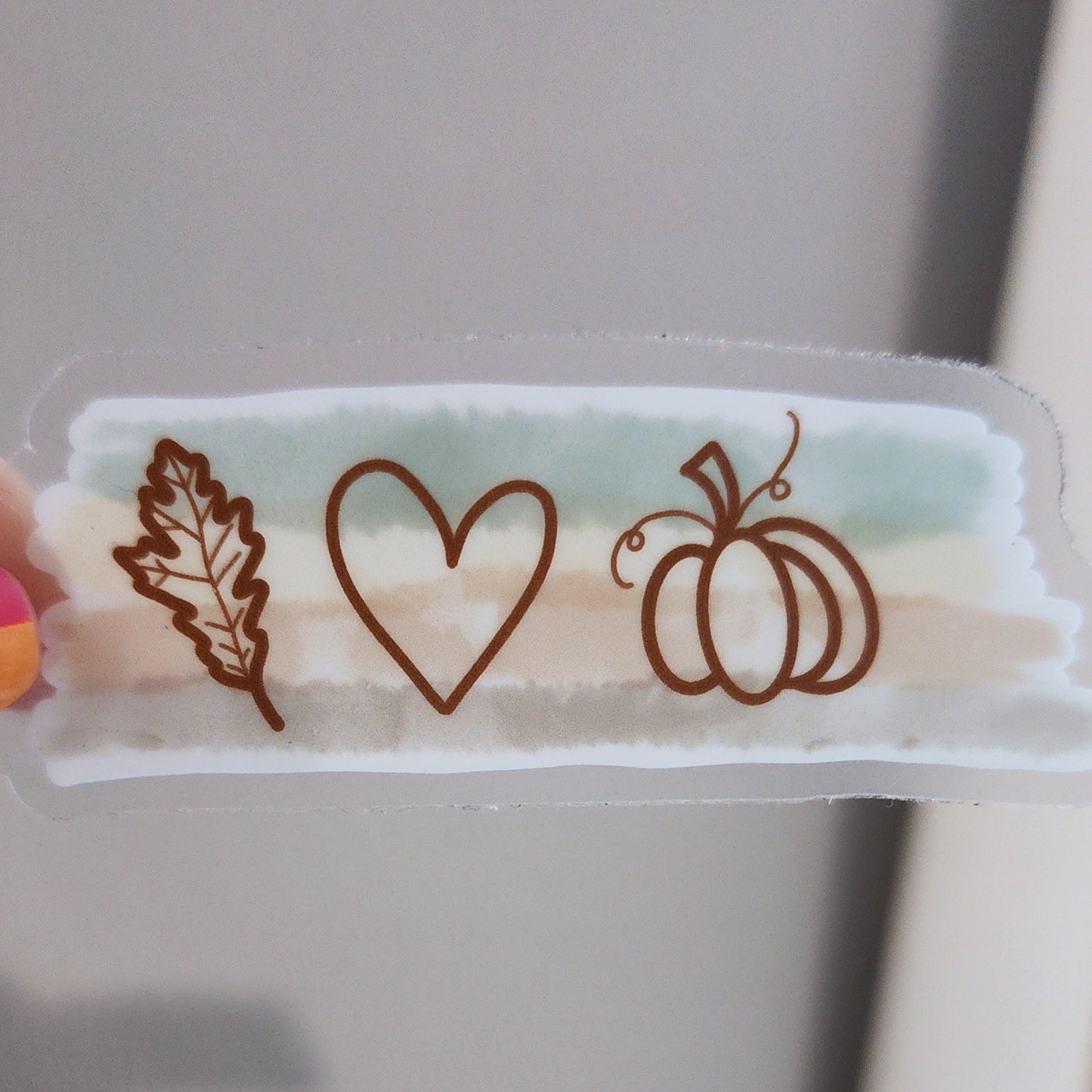 Minimal fall-themed sticker with pumpkin, heart, and leaf illustration on a transparent background without sticker backing showing transparency. 