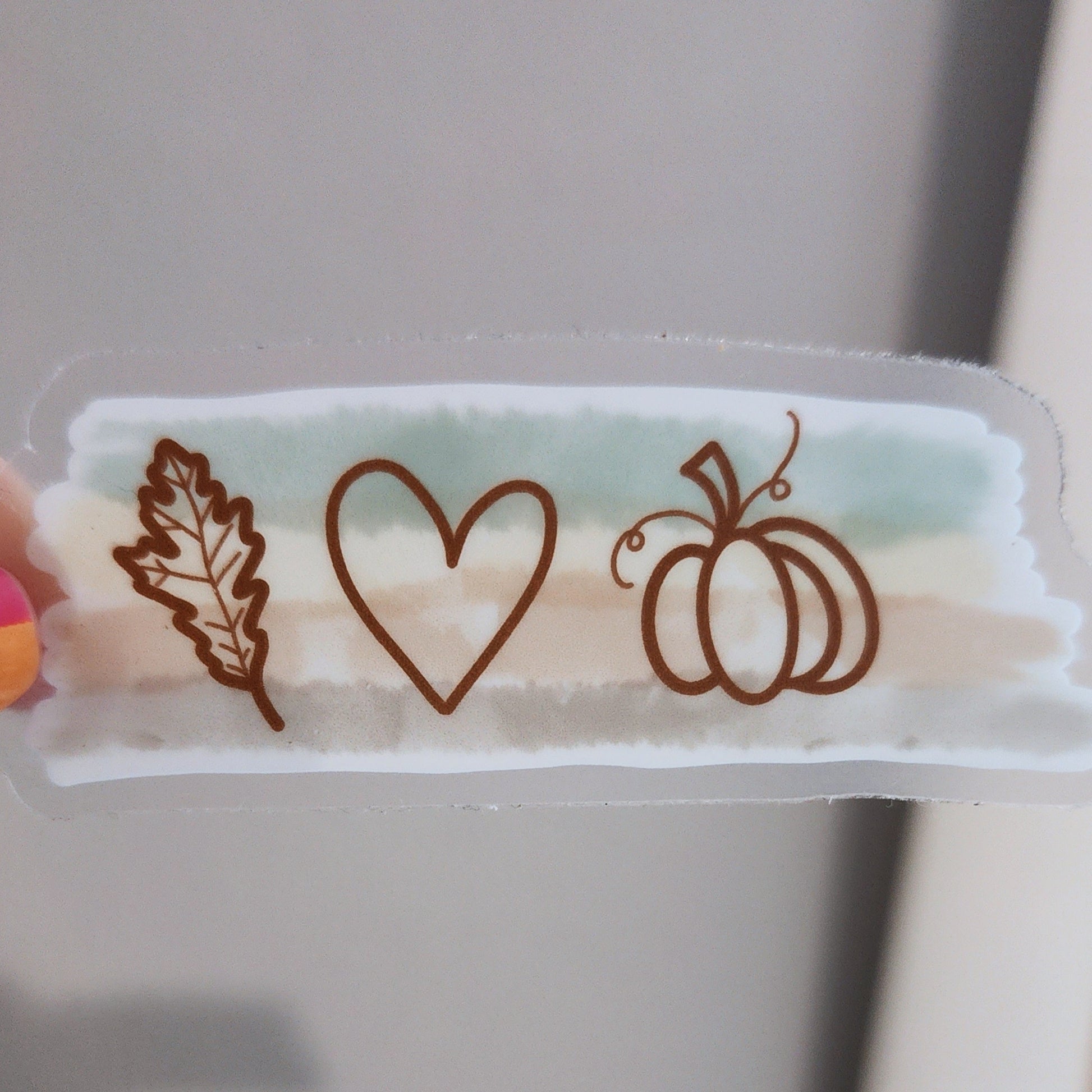 Minimal fall-themed sticker with pumpkin, heart, and leaf illustration on a transparent background without sticker backing showing transparency. 