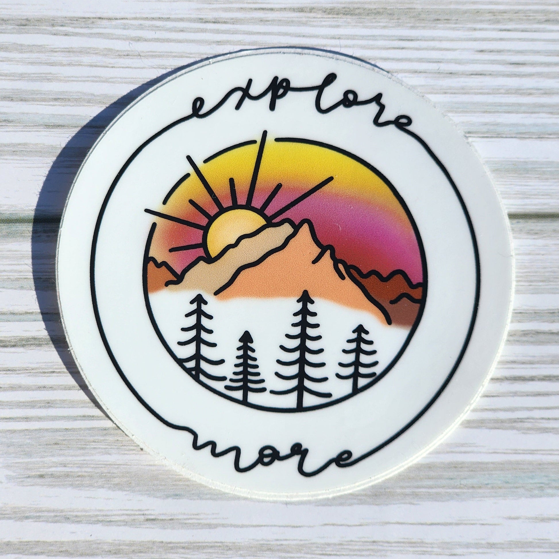 Vibrant mountain scape sticker with pink and orange sunset, framed with cursive 'Explore More'