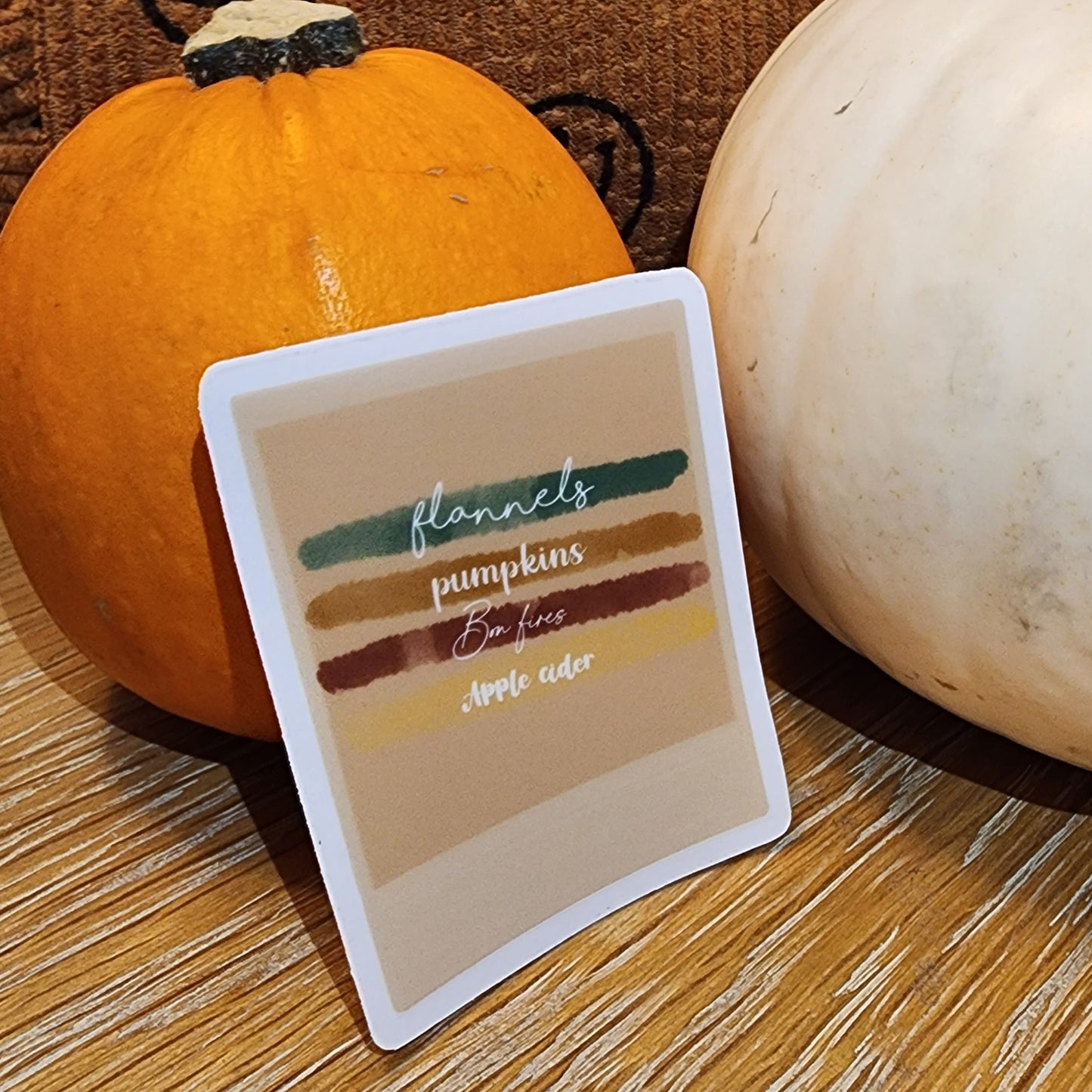 Cute autumn aesthetic waterproof sticker in Polaroid style with cozy fall checklist: Flannels, Pumpkins, Bonfires, Apple Cider leaned up against actual pumpkins