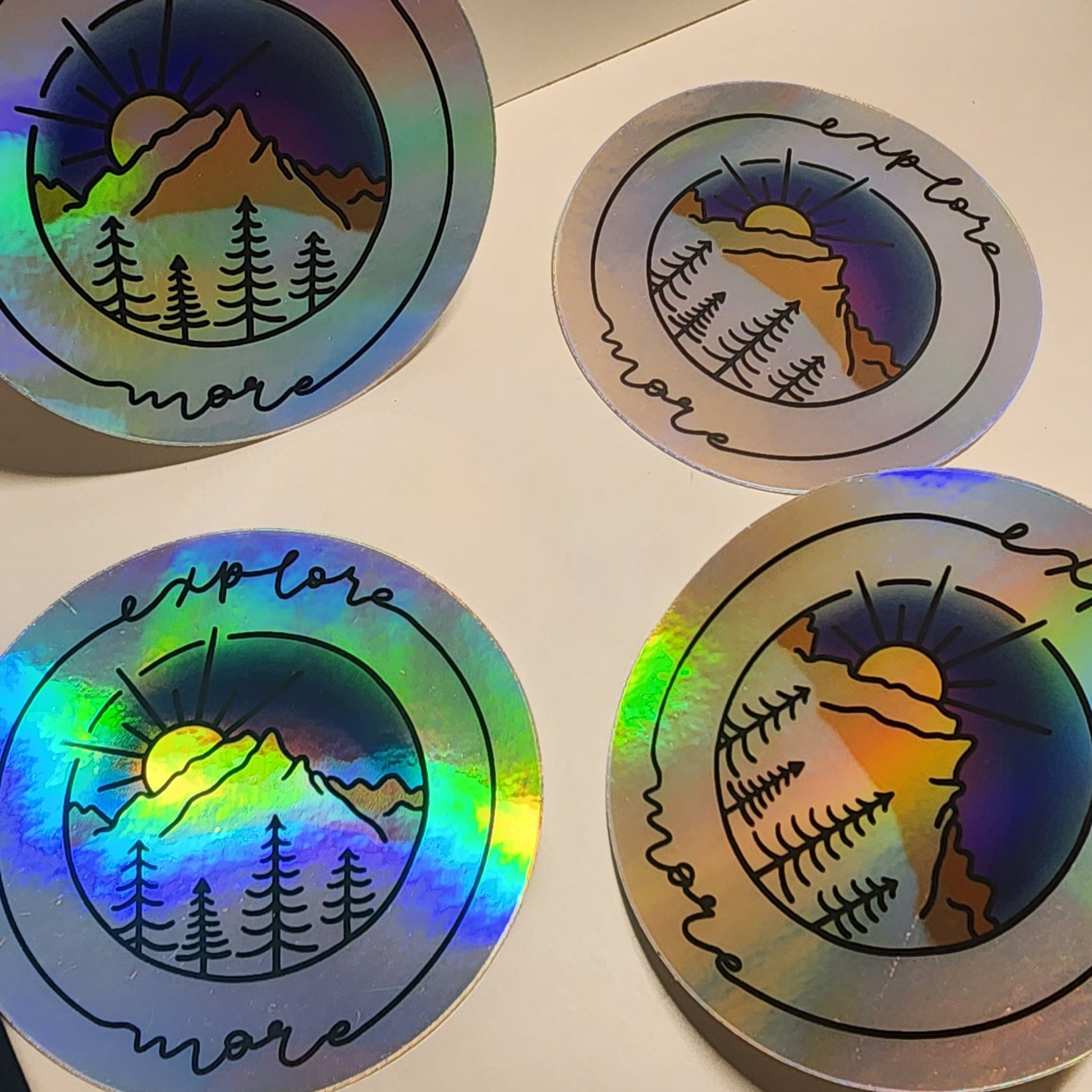 Vibrant mountain scape sticker with blue purple sunset, framed with cursive 'Explore More' on a holographic sticker