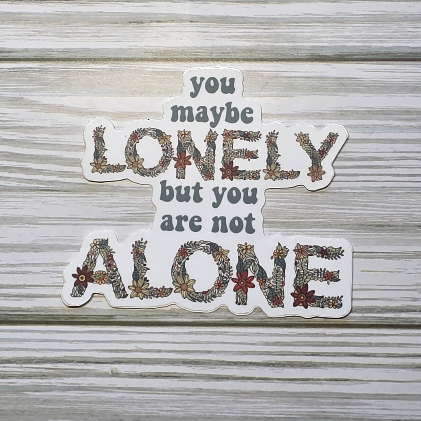 Typography design reading ‘You Maybe Lonely But You Are Not Alone,’ with the word ‘Lonely and Alone’ in decorative floral lettering.